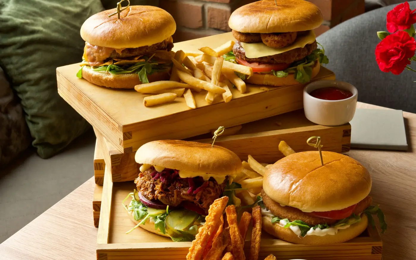 Three burgers and baskets of fries plated on wooden trays at a fast casual counter