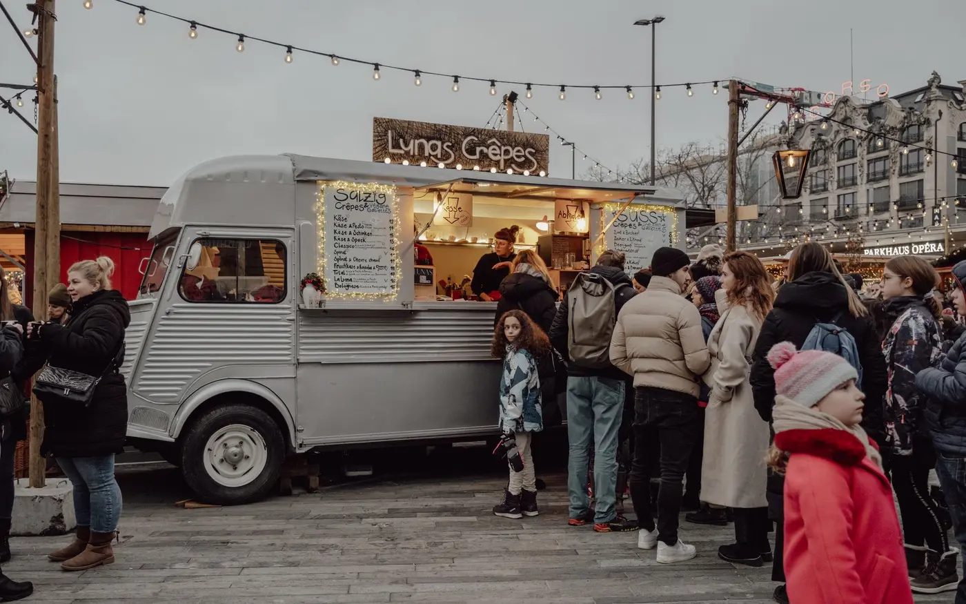 Customers queueing at a lit food truck serving from a street pitch in the evening