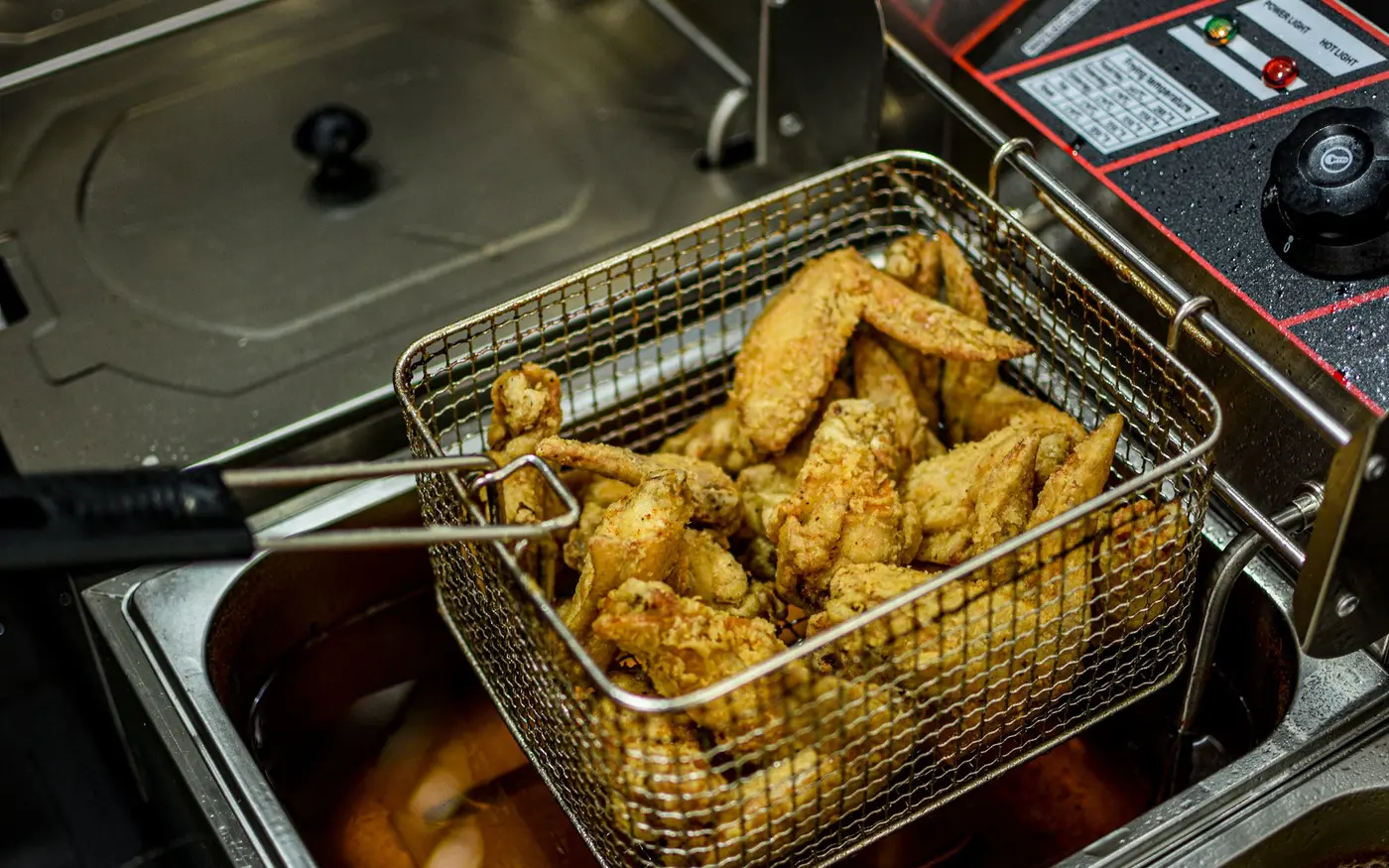 Golden fried chicken wings draining in a commercial fryer basket