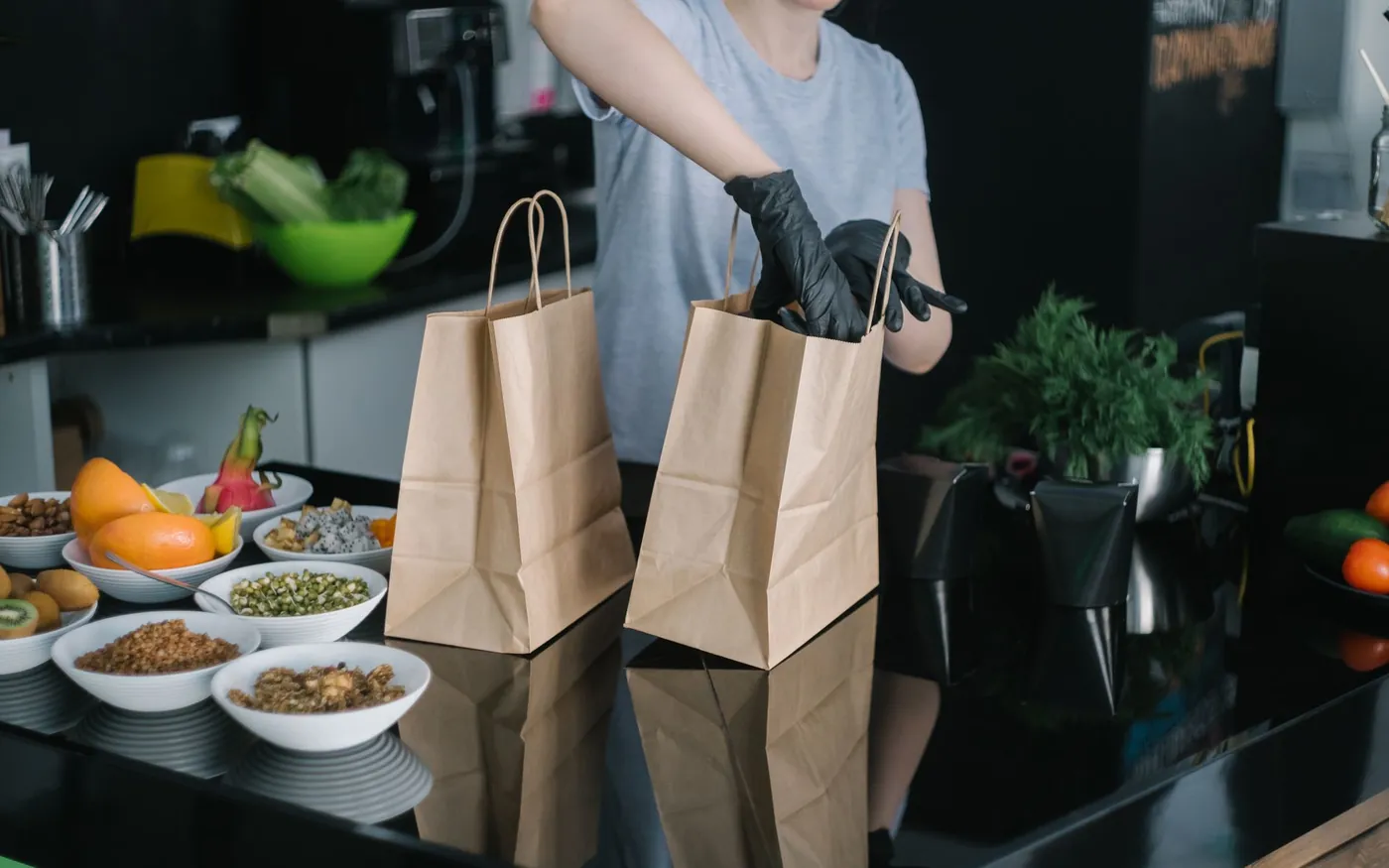 A kitchen worker in gloves packing takeout orders into paper bags on the counter